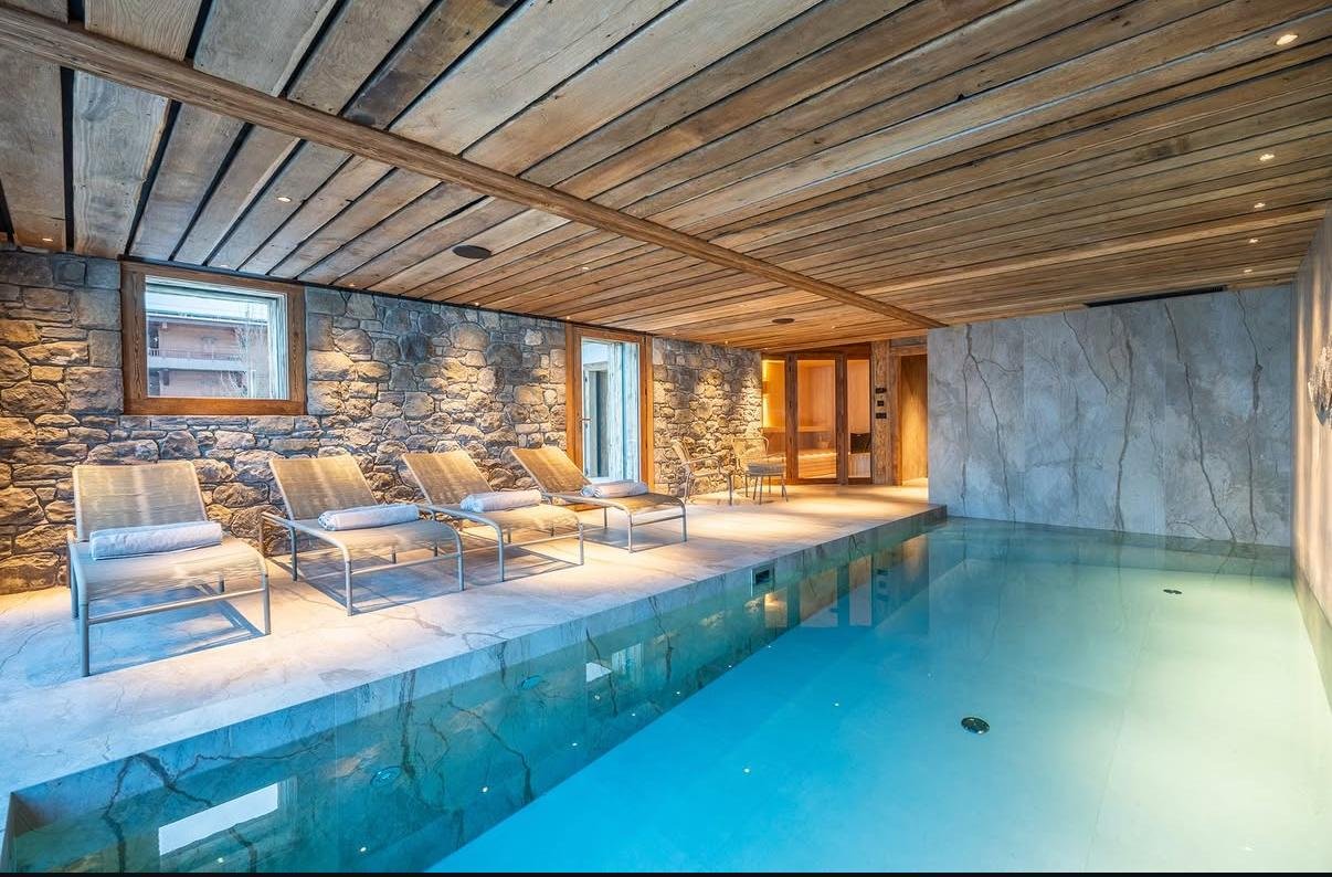Piscine intérieure avec carrelage en pierre, mur minéral et plafond en bois